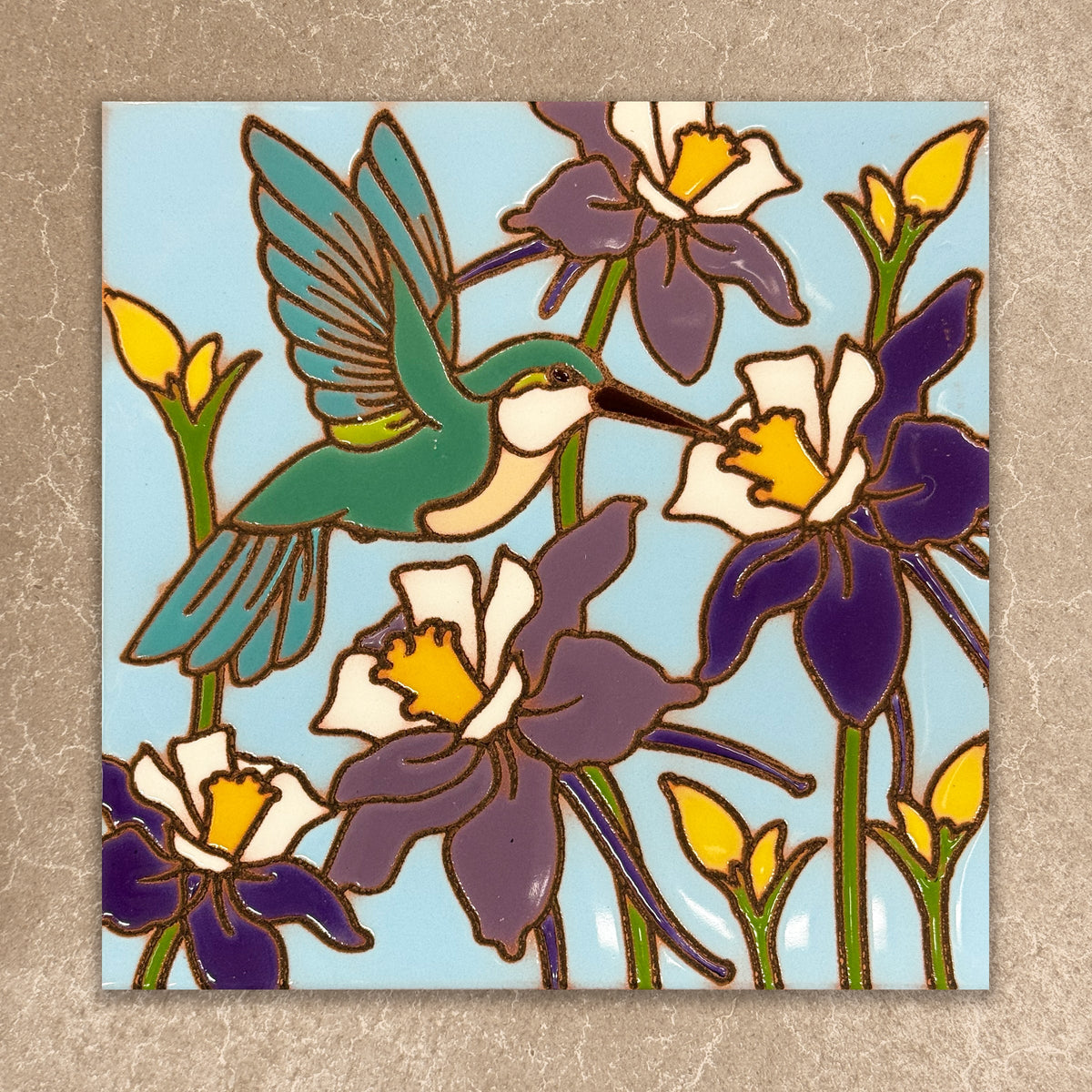 Decorative tile with a hummingbird and flowers on a blue background