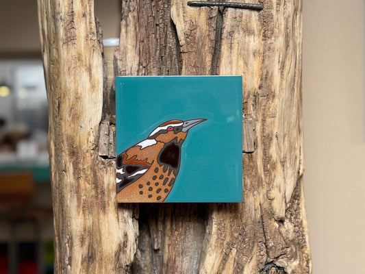 Square ceramic tile with a bird design on a wooden surface