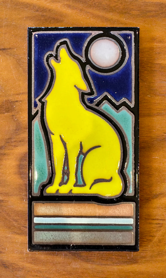 A hand glazed ceramic tile with a retro coyote design, featuring a yellow coyote silhouette against a blue background with a crescent moon.