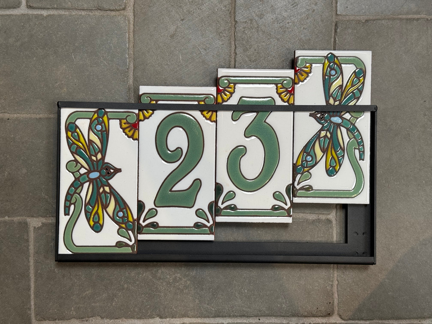 Set of decorative house number tiles with floral designs on a stone wall.