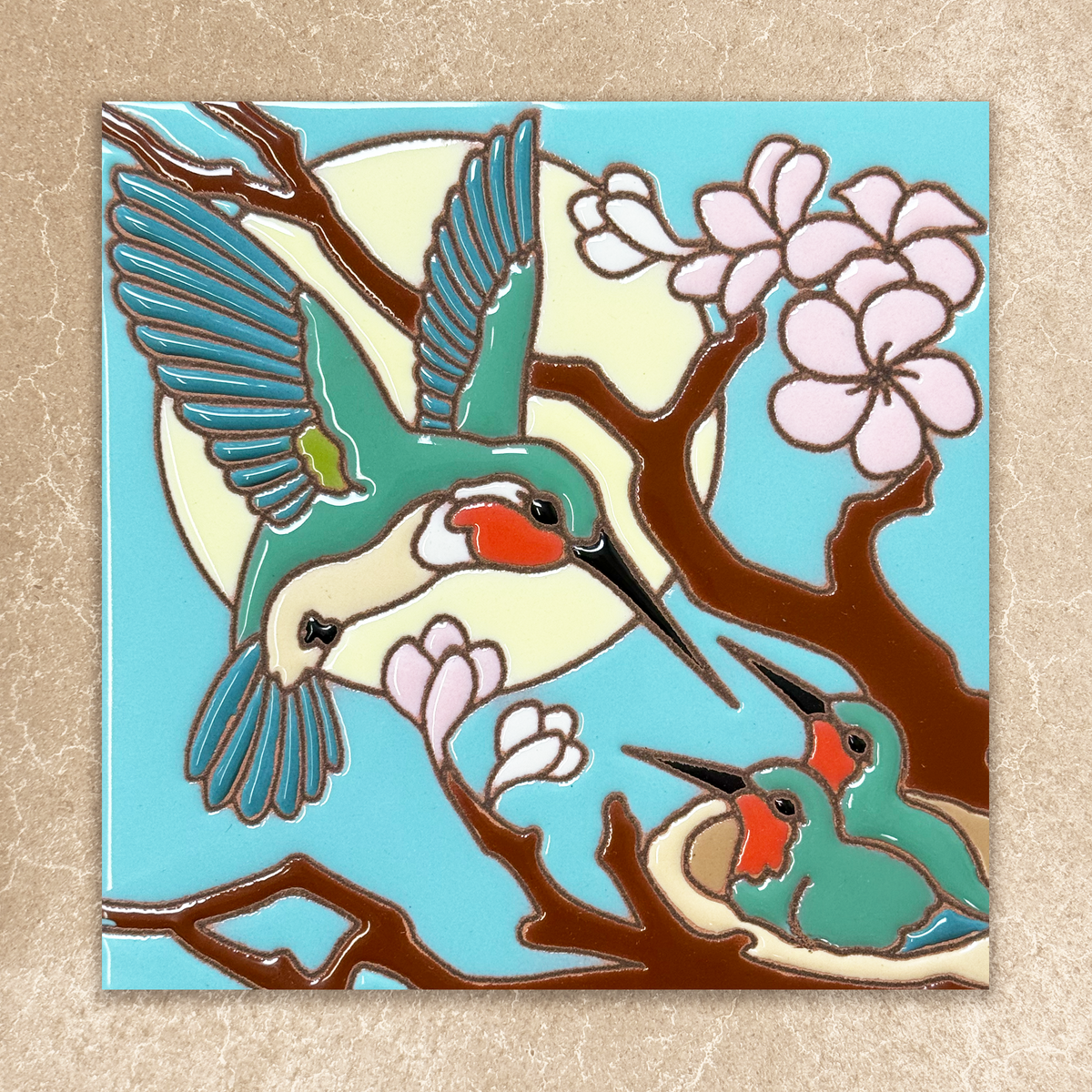 Decorative tile with a stylized illustration of a hummingbird and cherry blossoms on a blue background.