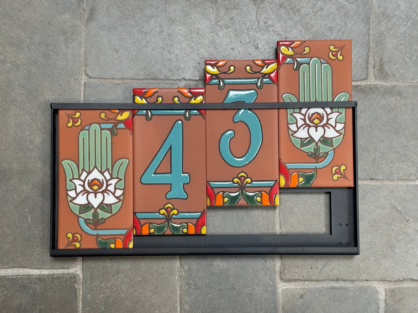 Decorative house number sign with floral designs on a stone wall.