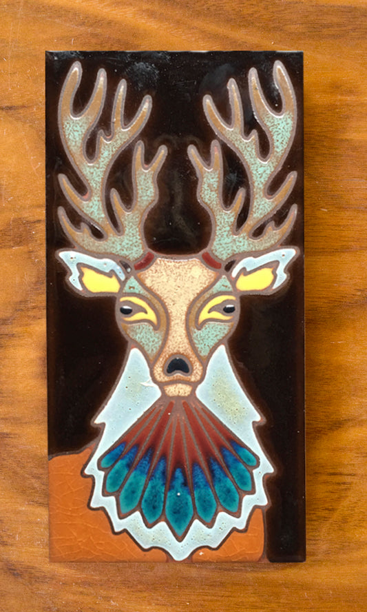 A hand-glazed ceramic tile shaped like a deer with multicolored eyes and a brown body on a dark background.