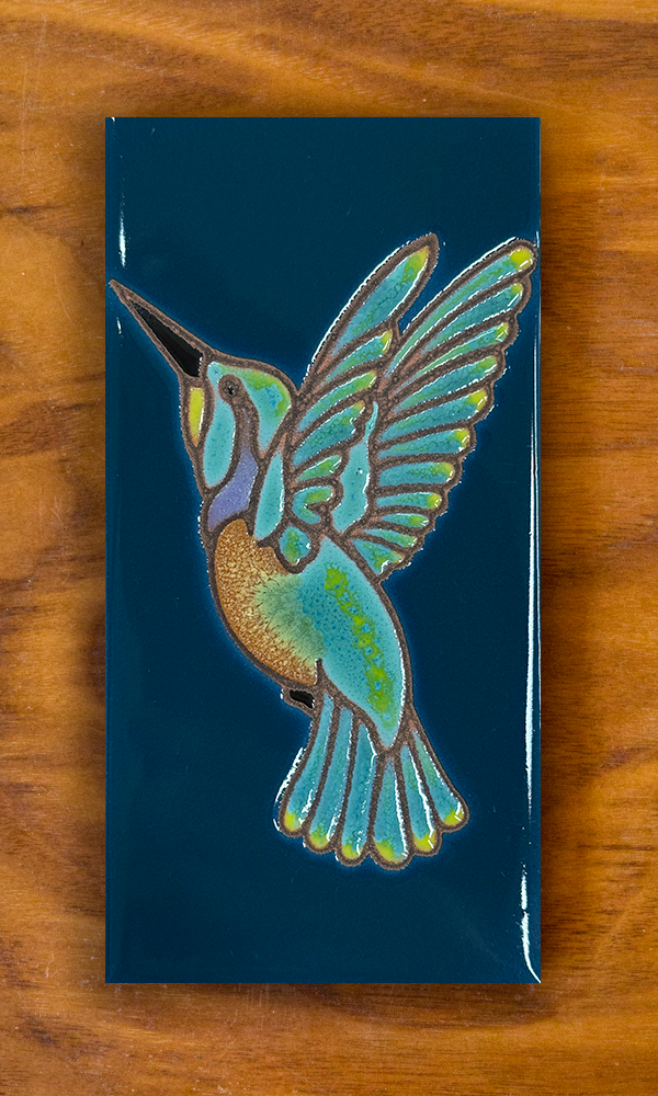 Ceramic hummingbird tile with dark turquoise background shown on a wooden board