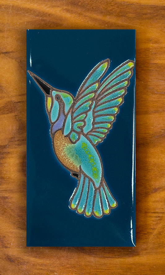 Ceramic hummingbird tile with dark turquoise background shown on a wooden board