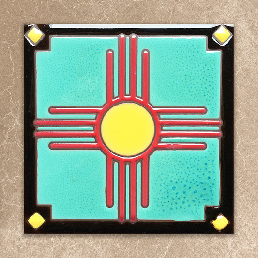 Decorative tile with a red and yellow zia symbol on a turquoise background, framed by black border with gold accents.