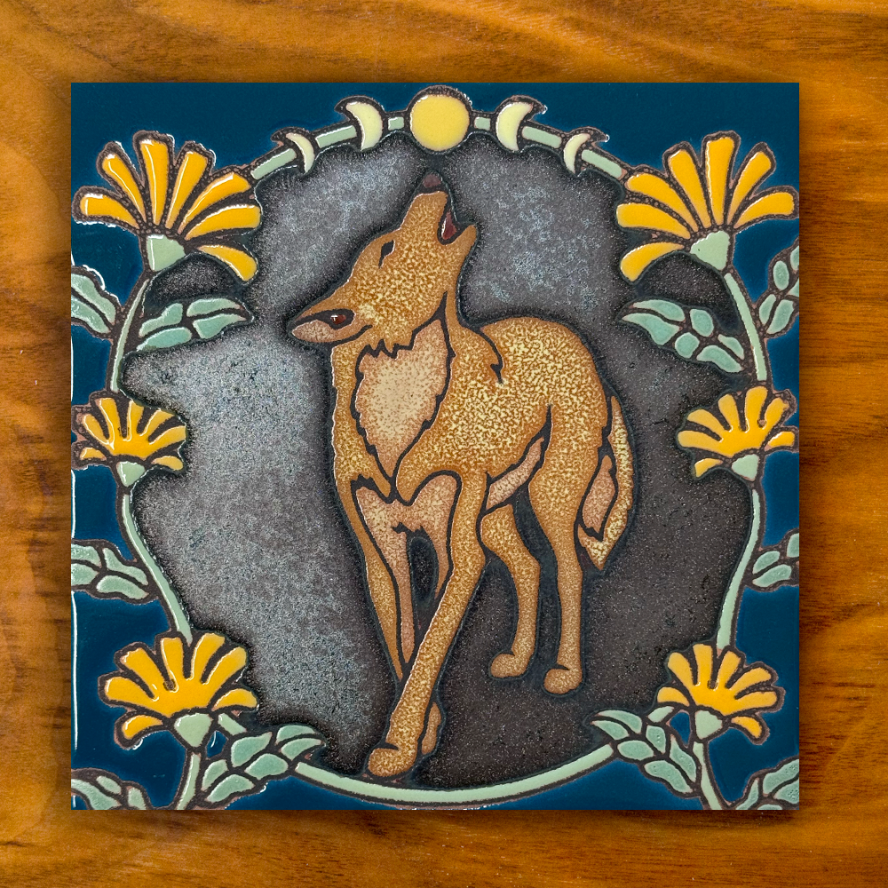 howling coyote ceramic tile on a shimmery black and blue with orange flowers, shown on a wooden background