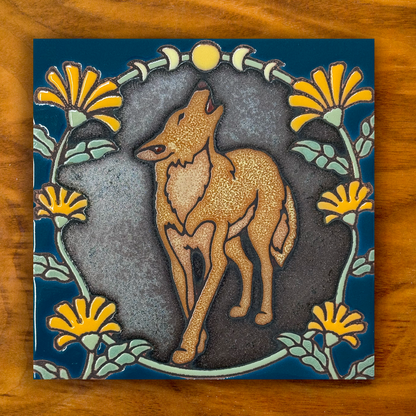 howling coyote ceramic tile on a shimmery black and blue with orange flowers, shown on a wooden background