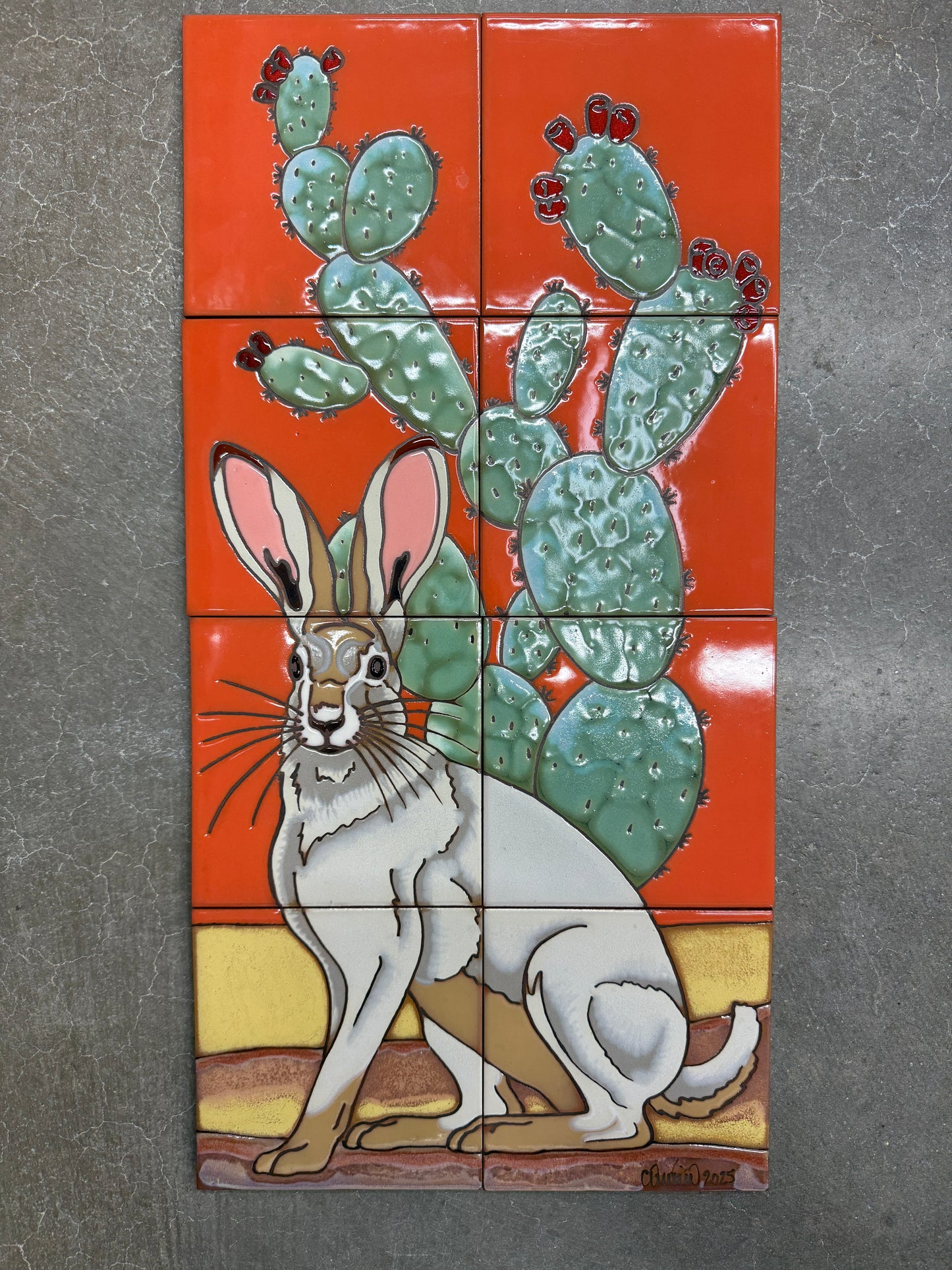 Decorative tile mural with a rabbit and cactus design on an orange background.