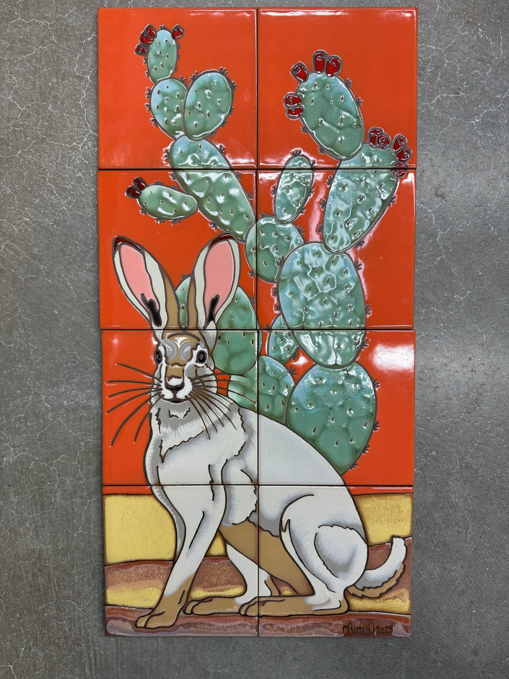 Decorative tile mural with a rabbit and cactus design on an orange background.