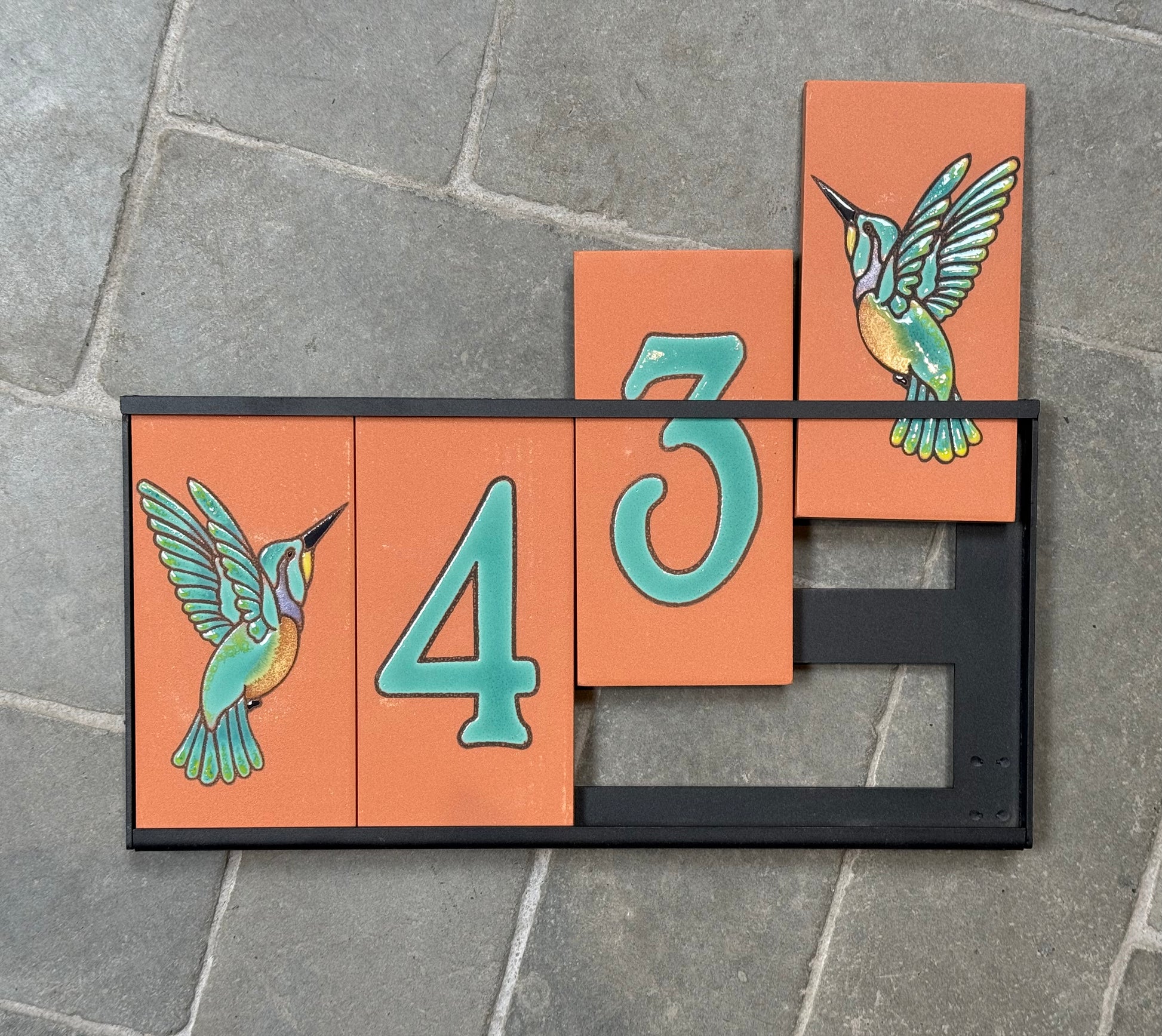 Decorative house number sign with hummingbird designs on a stone surface