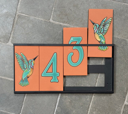 Decorative house number sign with hummingbird designs on a stone surface