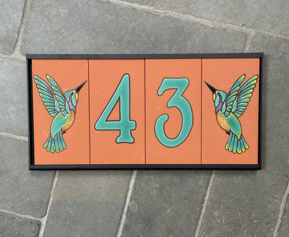 Decorative house number sign with hummingbirds on a stone pavement background