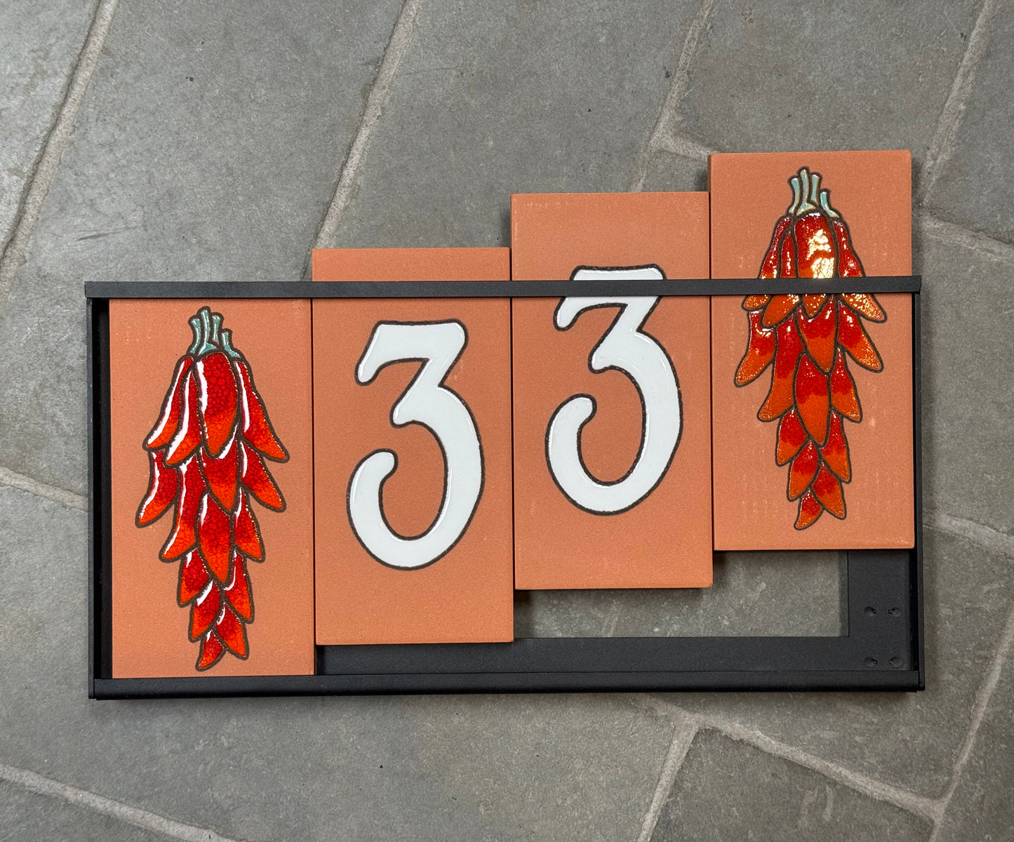 House number sign with red chili pepper design on a stone surface