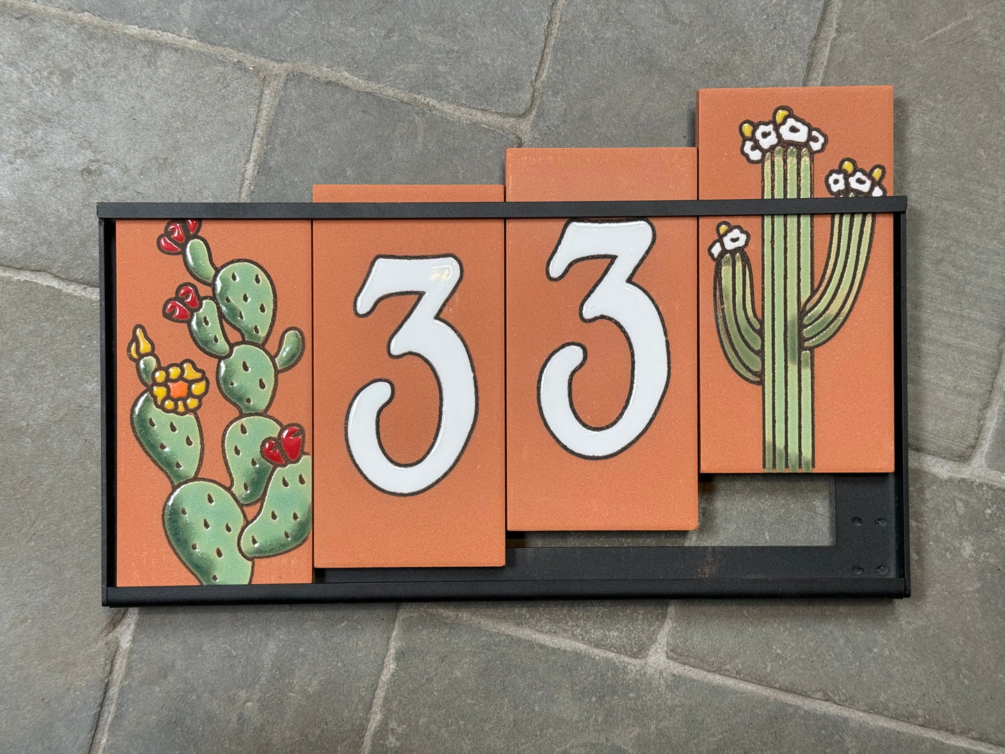Decorative house number sign with cacti on a stone surface