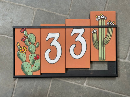 Decorative house number sign with cacti on a stone surface