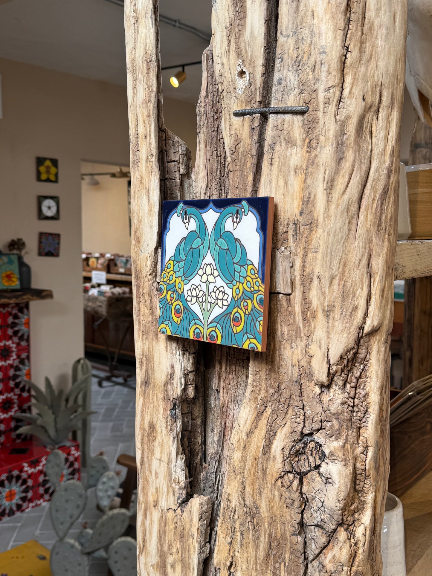 Decorative tile with peacock design attached to a wooden surface