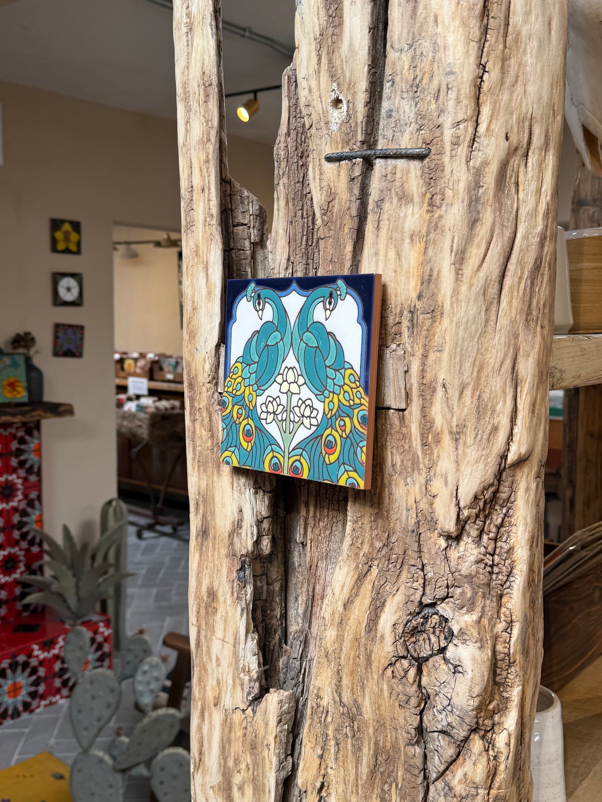 Decorative tile with peacock design attached to a wooden surface