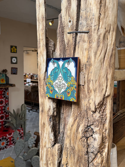 Decorative tile with peacock design attached to a wooden surface