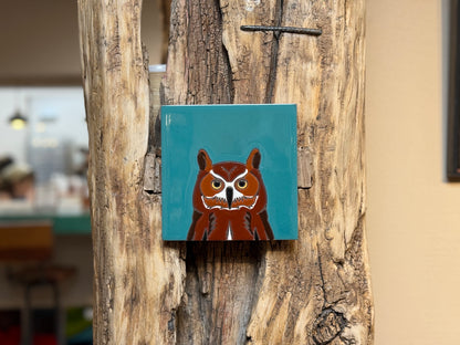 Square tile with an owl design on a wooden surface