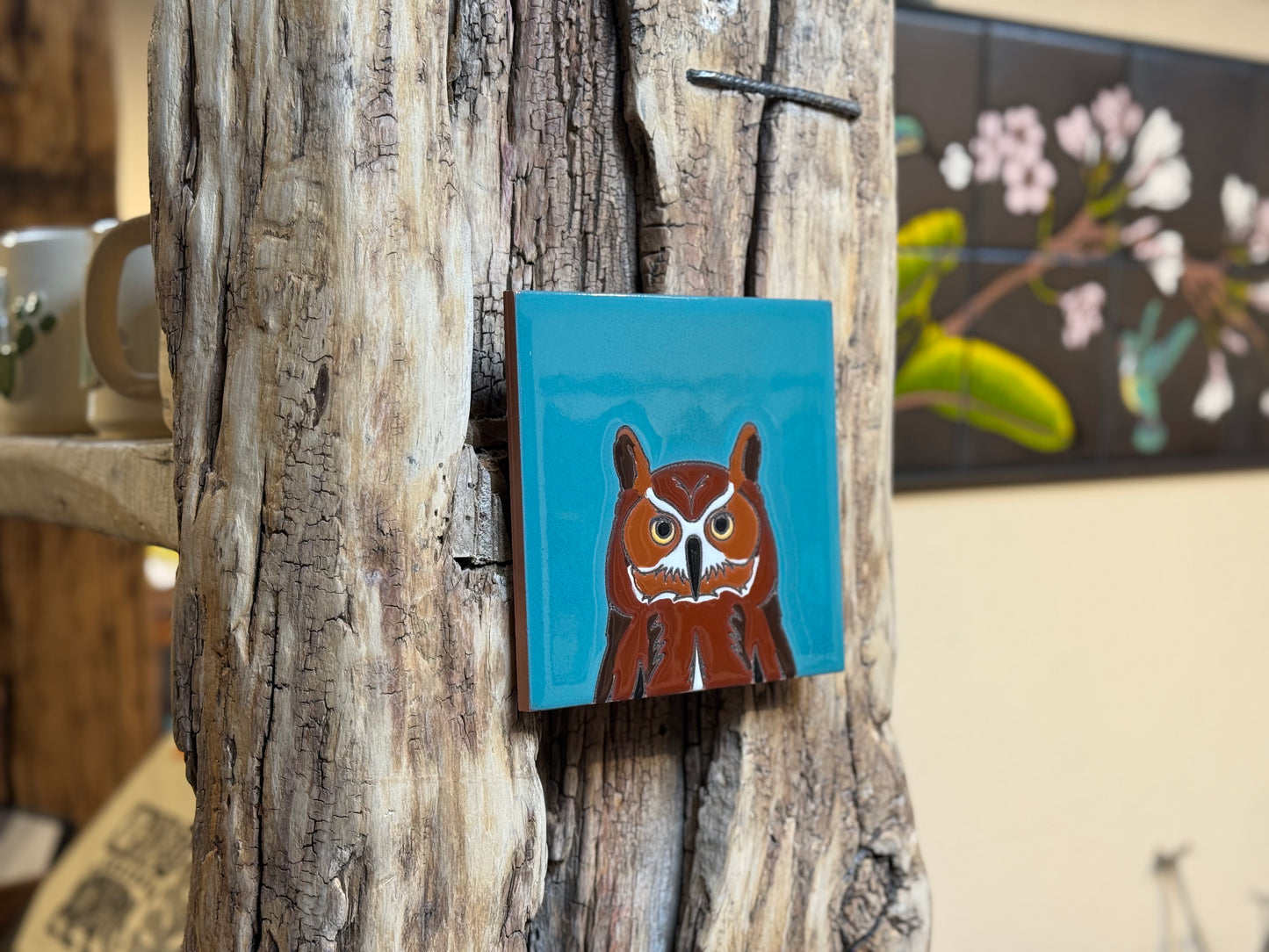Small square painting of a brown creature with white face on a blue background, attached to a textured wooden surface.