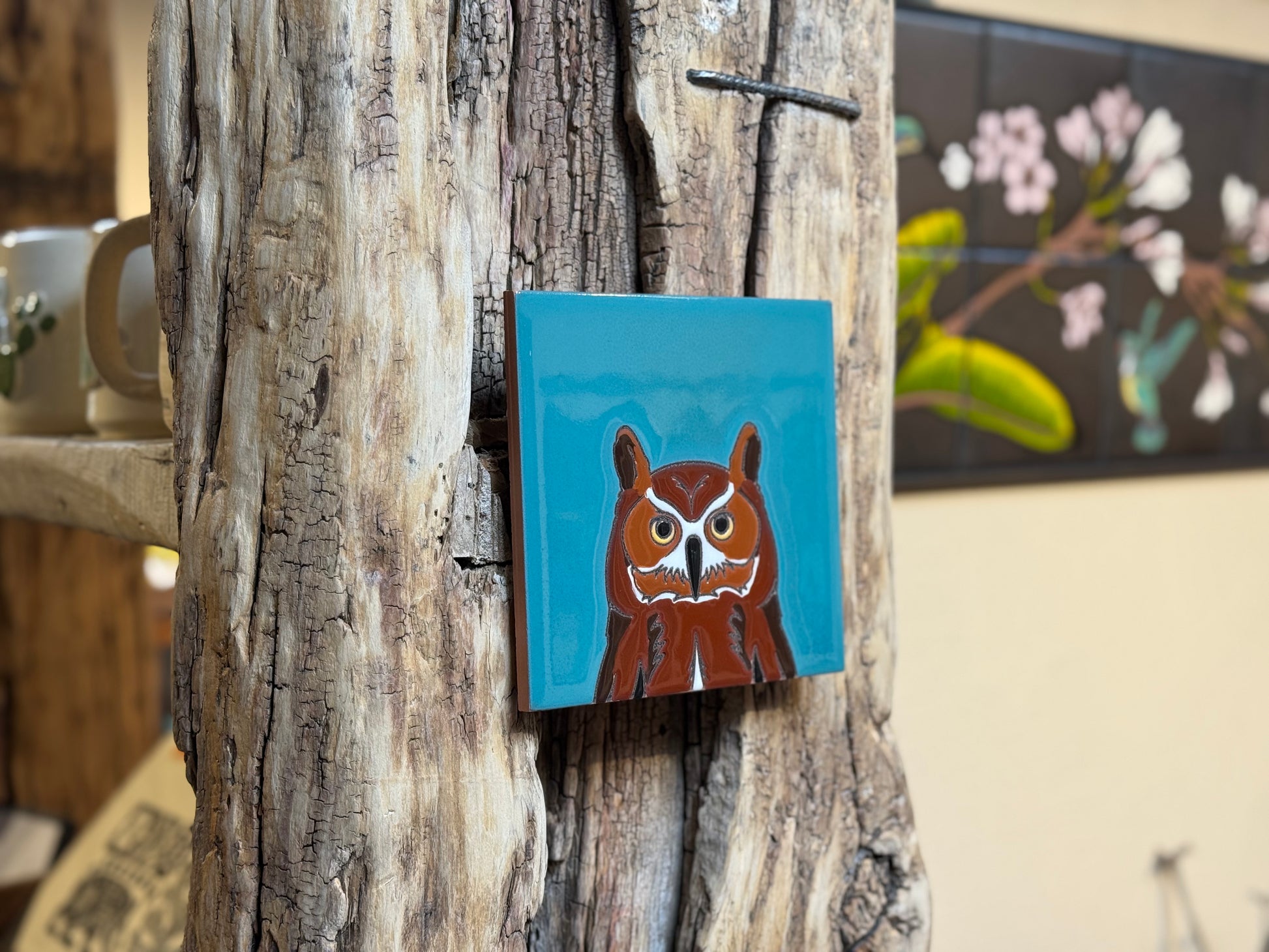 Small square painting of a brown creature with white face on a blue background, attached to a textured wooden surface.