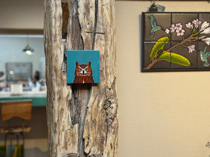 Decorative owl painting on a wooden surface with another artwork in the background.