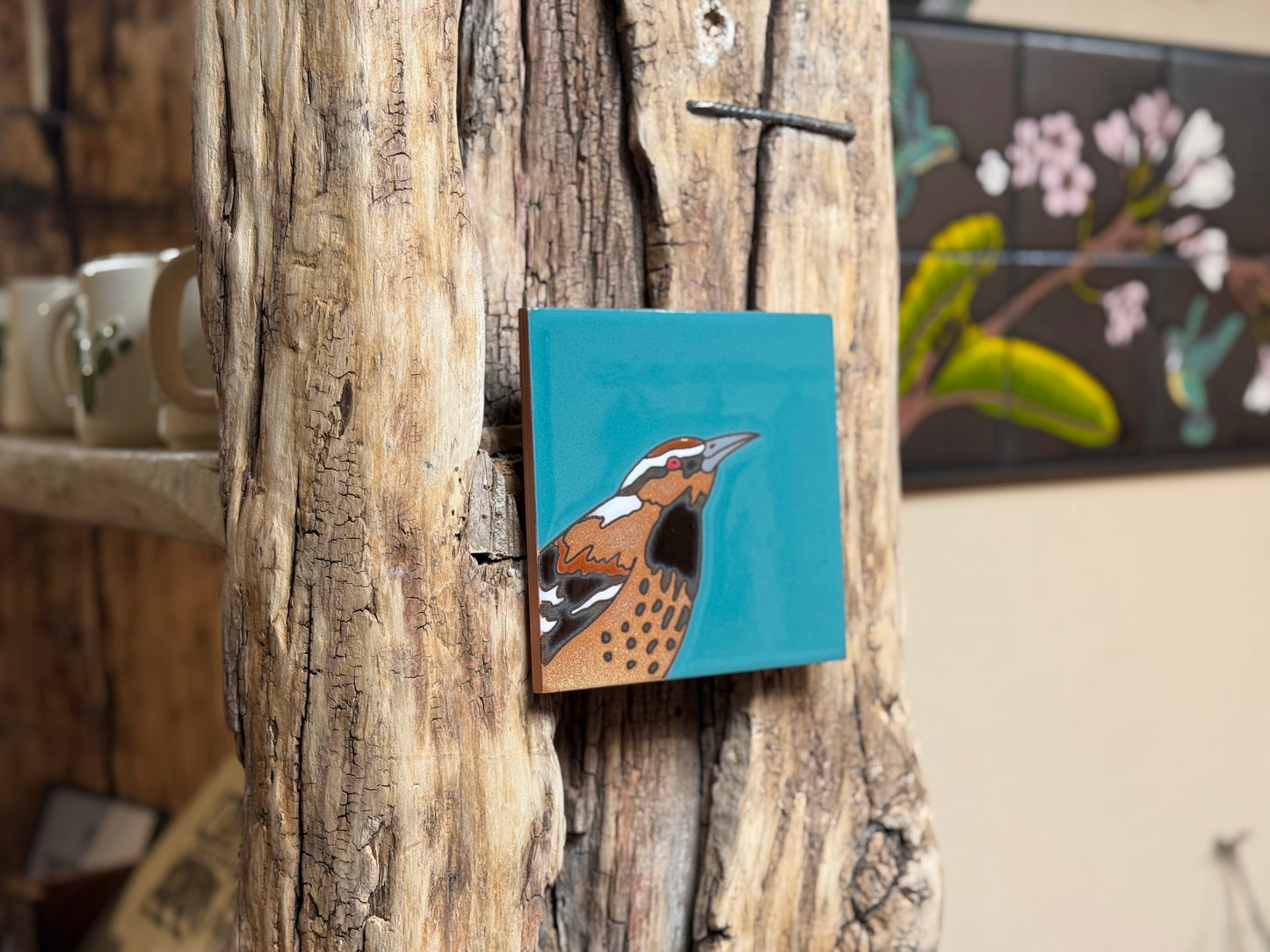 Small square painting of a bird on a wooden surface with a blurred background