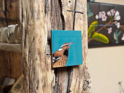 Small square painting of a bird on a wooden surface with a blurred background