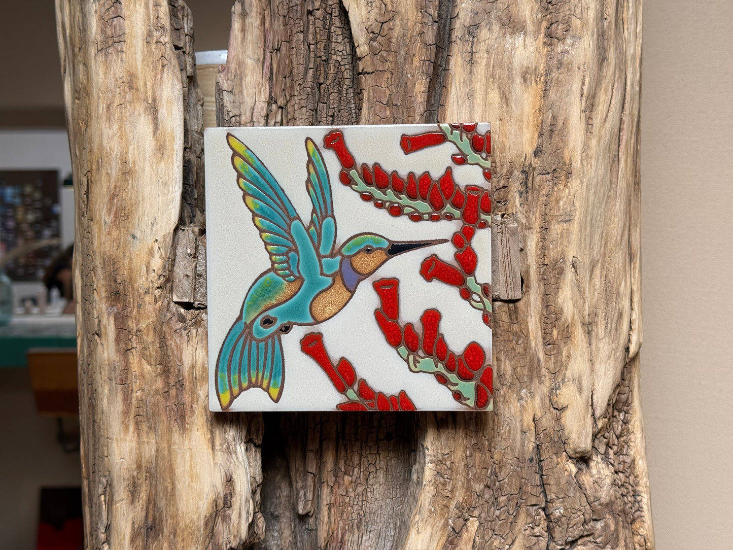 Decorative tile with a hummingbird and red berries design on a wooden surface