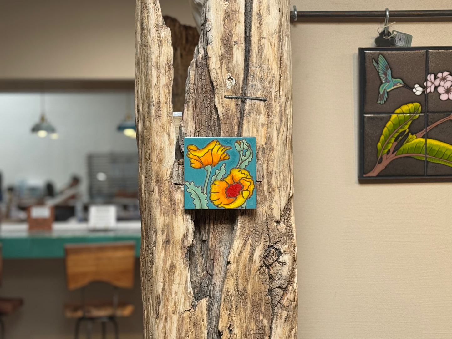 Decorative tile with floral design attached to a wooden surface, with a blurred indoor setting in the background.