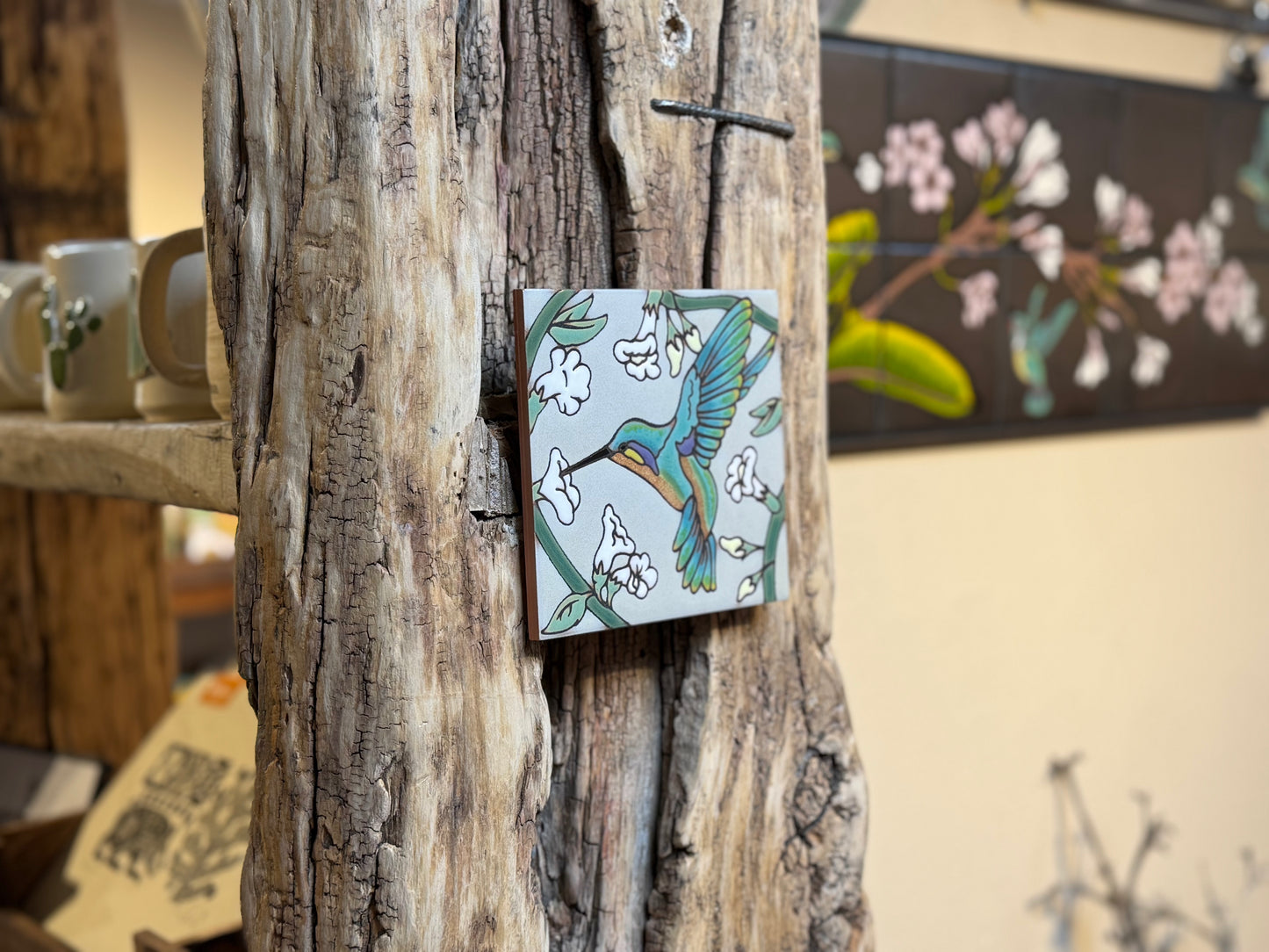 Decorative tile with a hummingbird design attached to a wooden surface.
