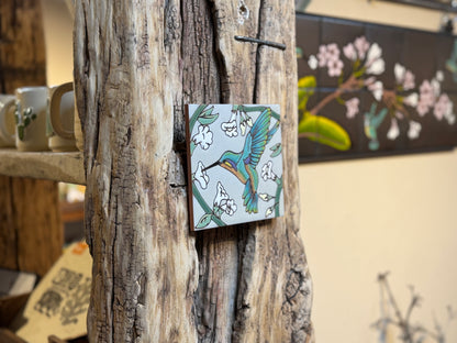 Decorative tile with a hummingbird design attached to a wooden surface.