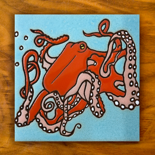 red octopus ceramic tile with blue background shown on a wooden table