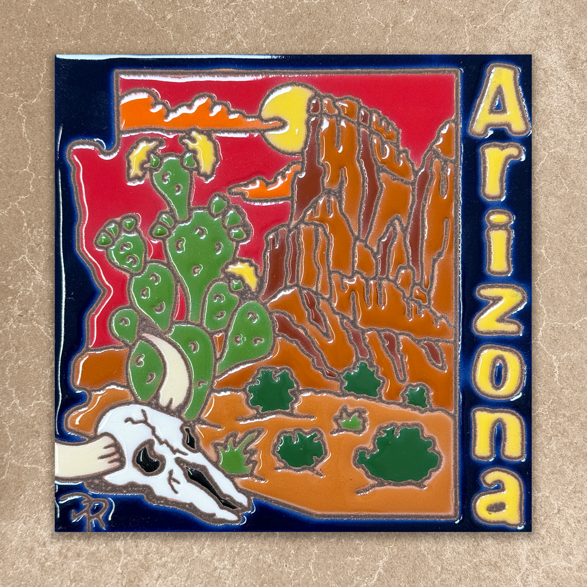 ceramic tile with Arizona landscape design featuring cacti, mountains, and skull on a beige background.