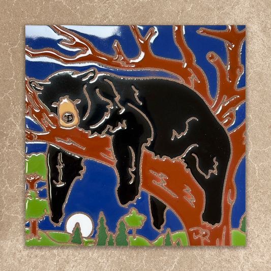 ceramic tile with a black bear climbing a tree against a blue sky.