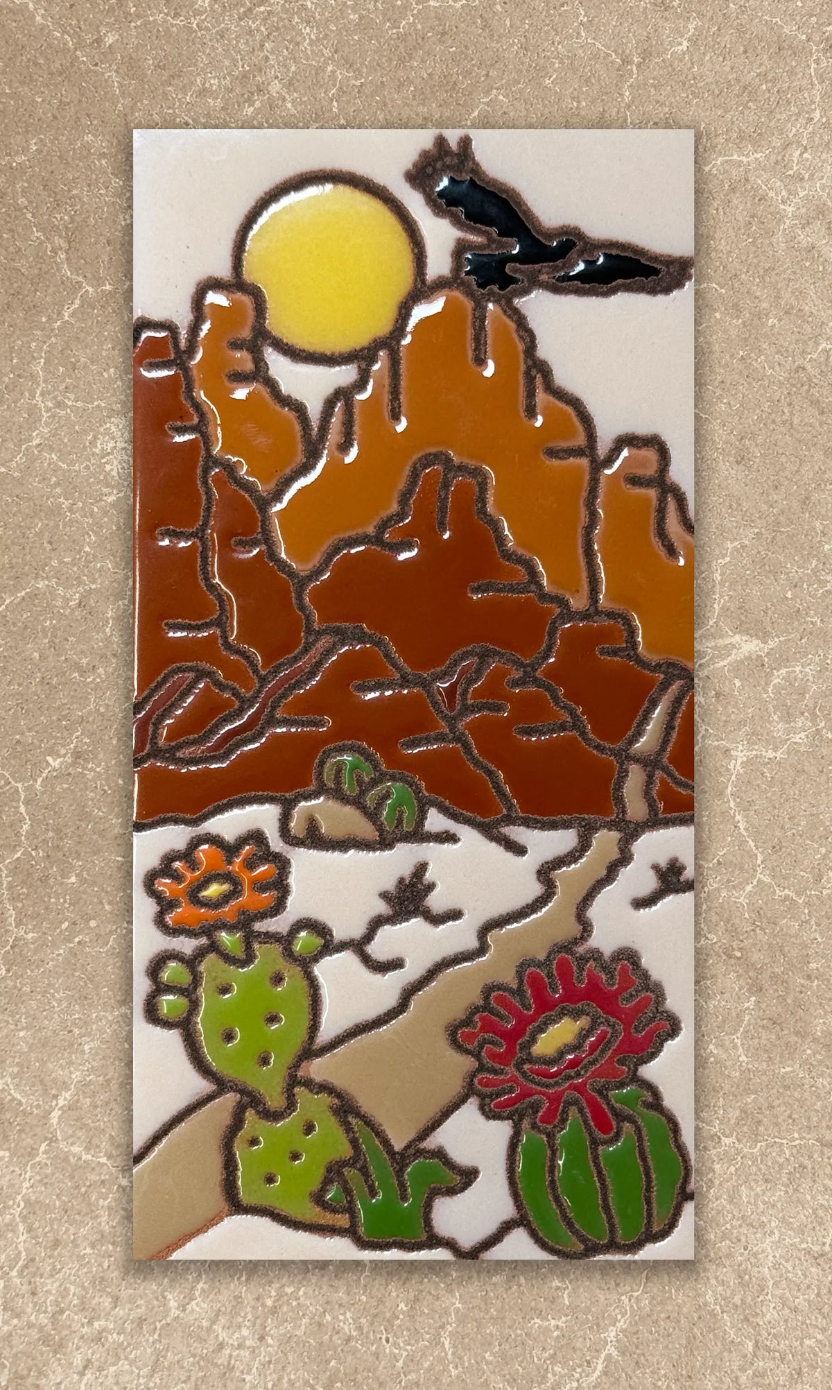 Decorative tile with desert landscape design featuring mountains, sun, cacti, and birds on a beige background.