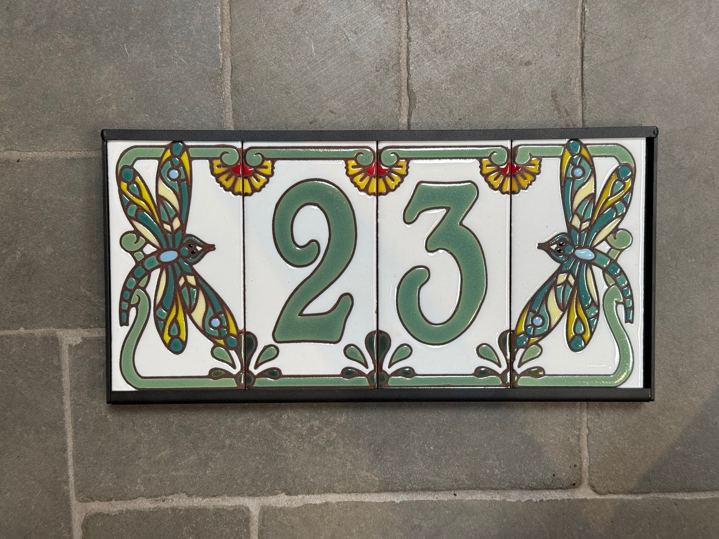Decorative tile with the number 23 and dragonfly designs on a stone wall.