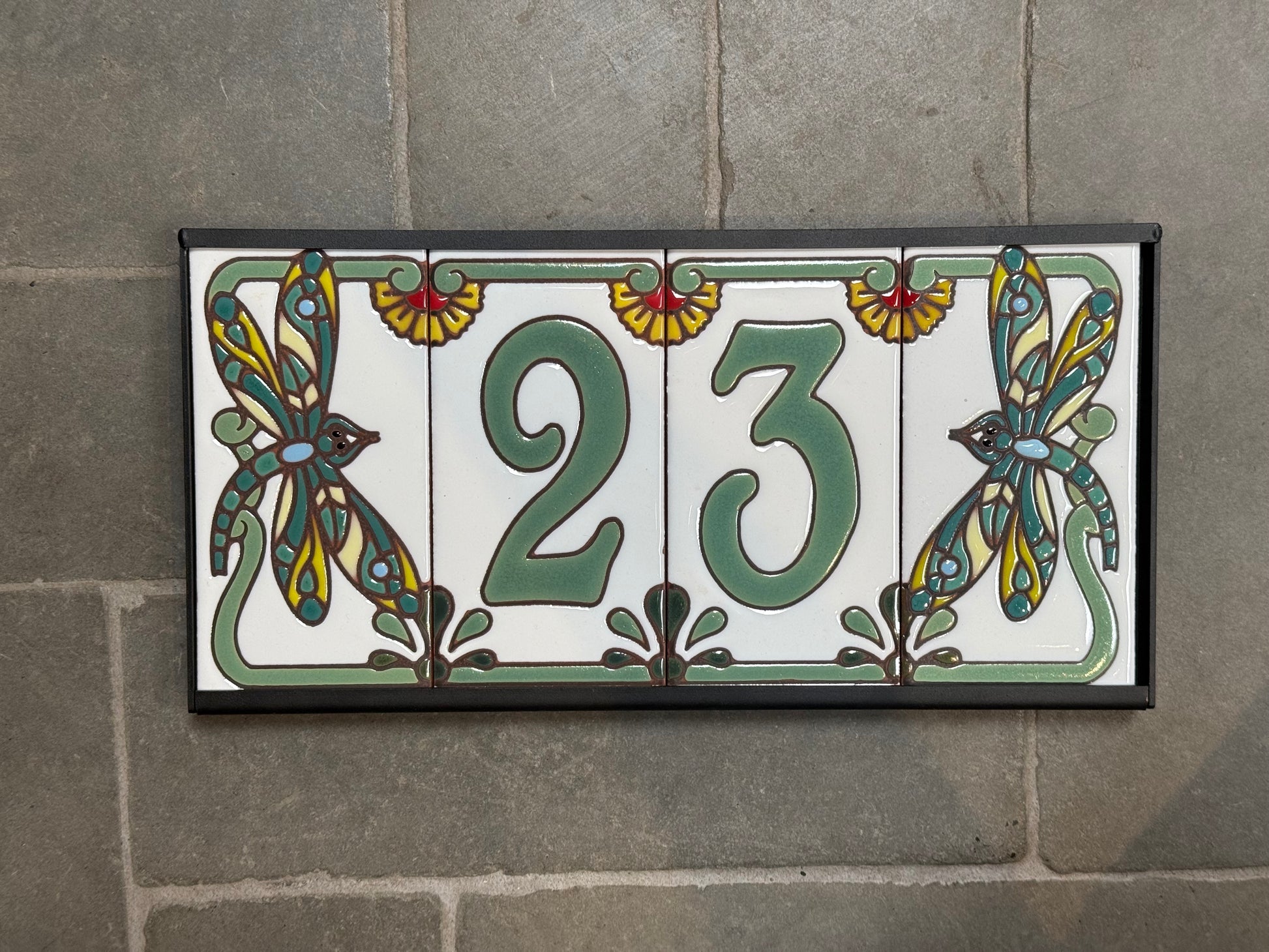 Decorative tile with the number 23 and dragonfly designs on a stone wall.