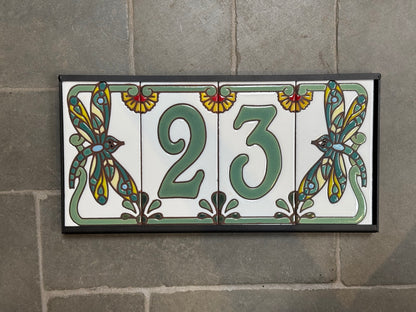 Decorative tile with the number 23 and dragonfly designs on a stone wall.