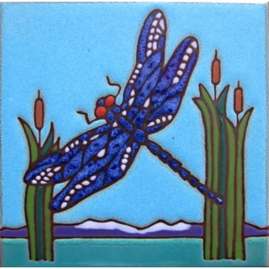 A square ceramic tile featuring a stylized folk-art illustration of a blue dragonfly perched on green reeds with brown cattails against a light blue sky and teal water.