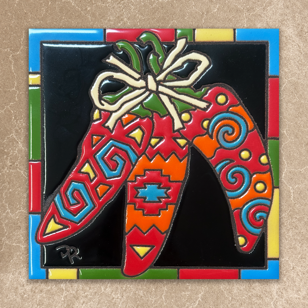 Colorful ceramic tile with decorative patterns and a bow on a multicolored border.