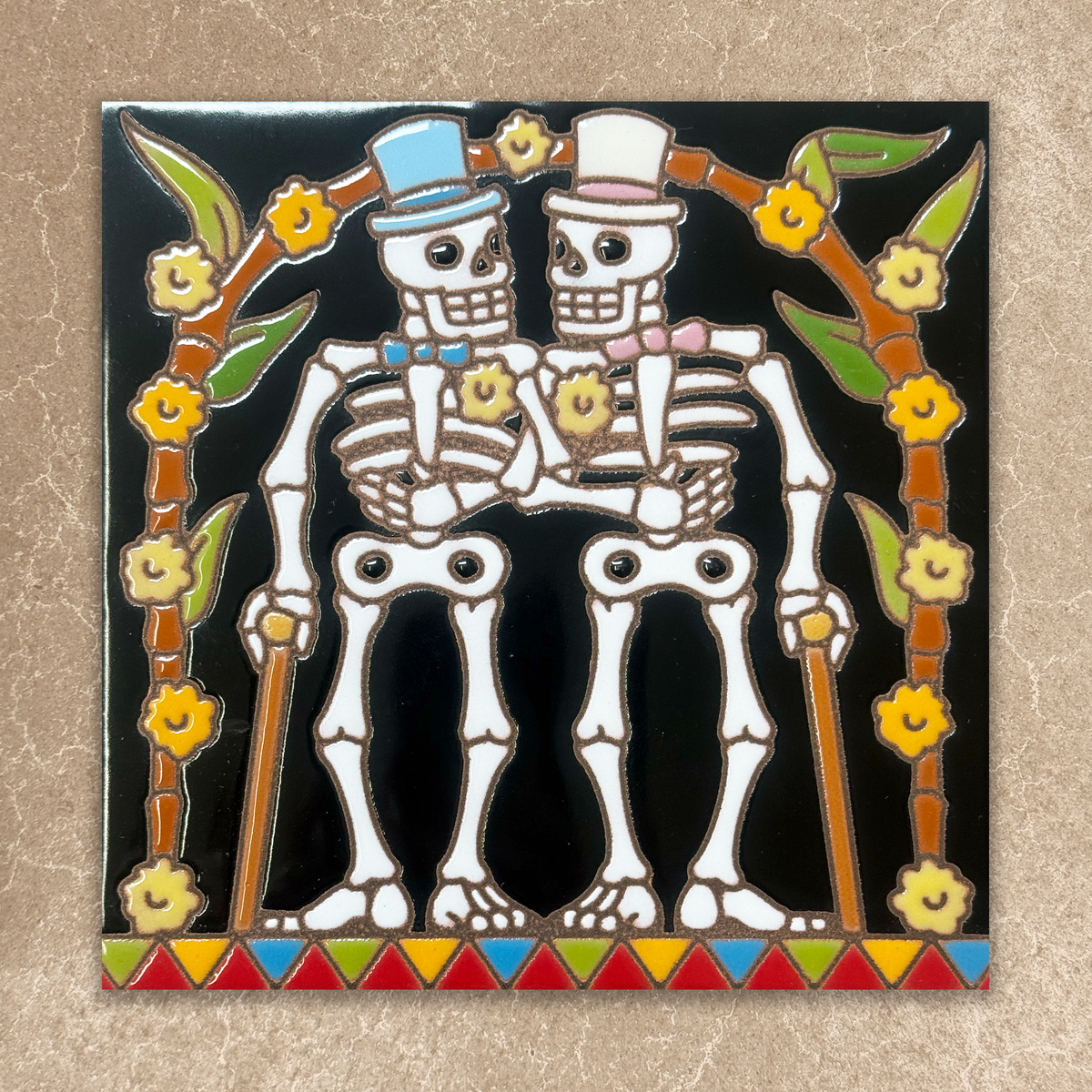 Decorative tile with skeletons holding hands and colorful border on a beige background