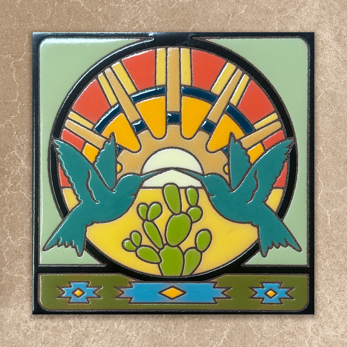 Decorative tile with two blue birds, a cactus, and a colorful sun design on a beige background.