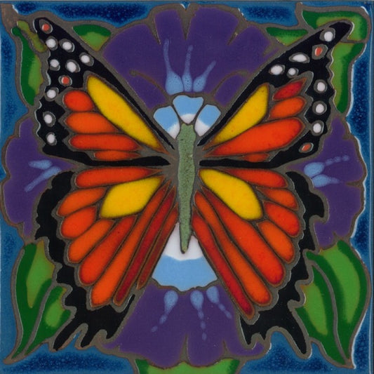 A square decorative tile or art piece featuring a stylized butterfly over a purple flower. The butterfly has orange, yellow, black, and light blue wings, set against green leaves and a blue border.