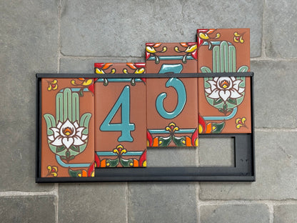 Decorative house number sign with floral designs on a stone wall.