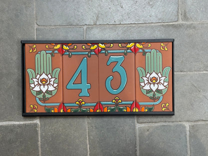 Decorative house number sign with flowers and hamsa hands on a stone wall background