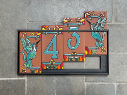 Decorative house number sign with hummingbirds on a stone wall