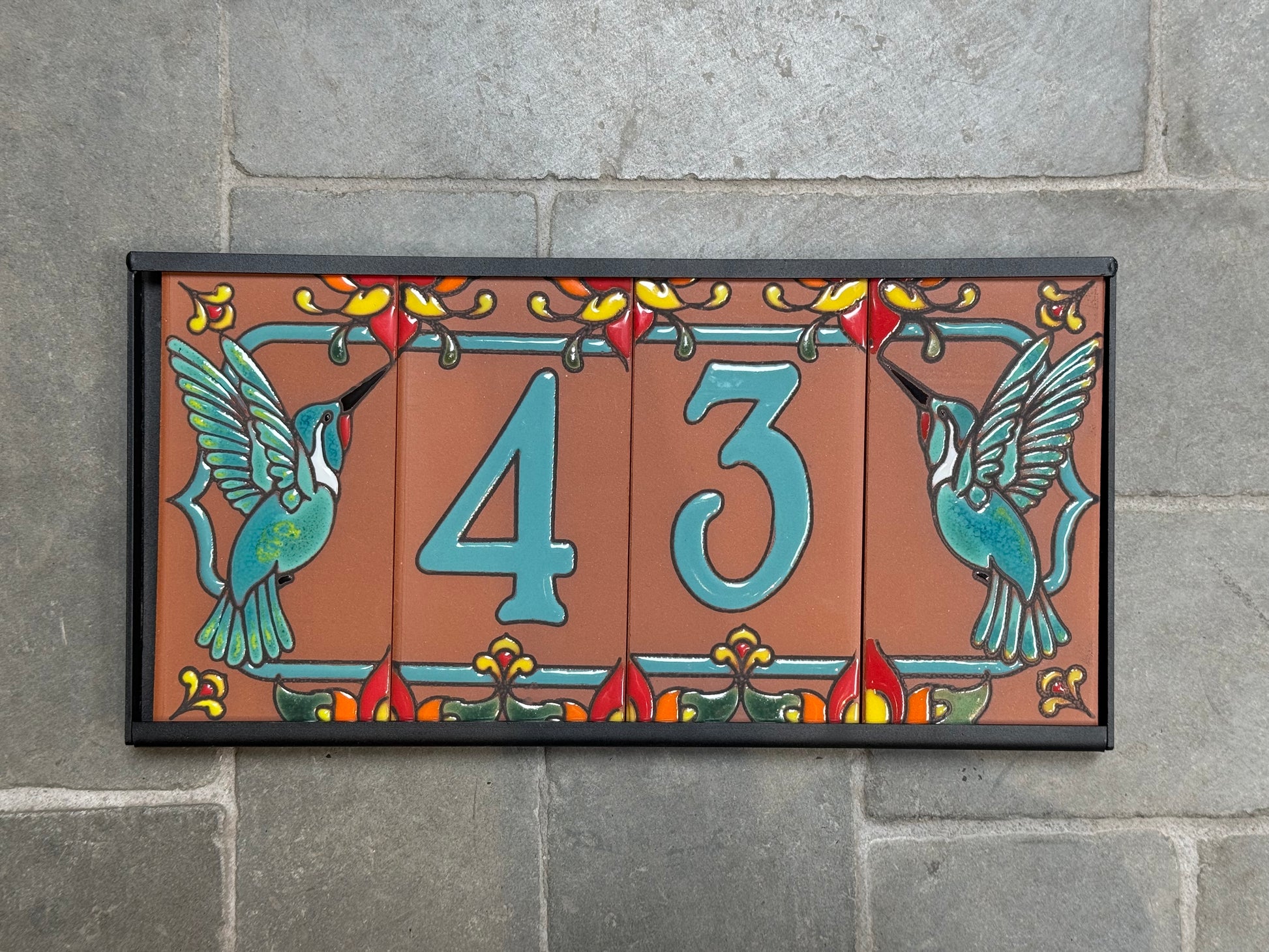 Decorative house number sign with '43' and hummingbirds on a stone wall background