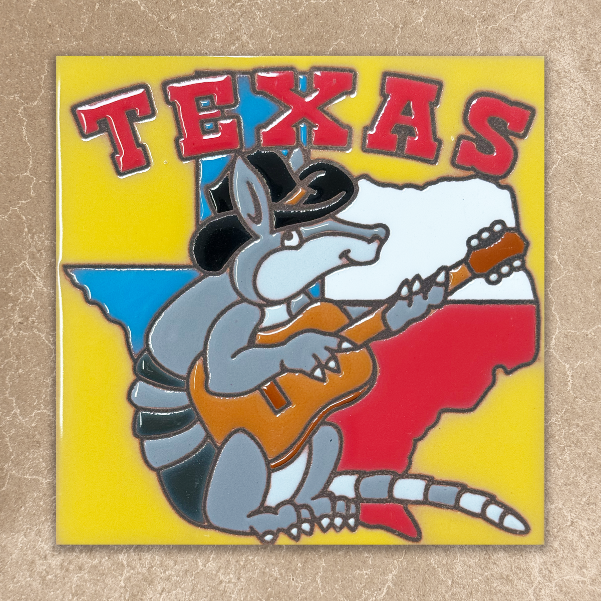 Decorative tile with a Texas-themed design featuring a lizard playing a guitar on a yellow background.